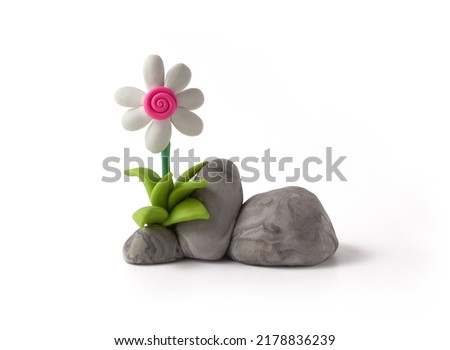 Flower with white petals and fuchsia center on stone with cracked texture and grass made of plasticine. Set of flower and rocks isolated on white background. Handmade stone and daisy. 3d artwork