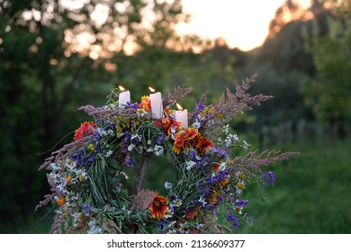 Flower wreath with burning candles on evening meadow. Summer Solstice Day, Midsummer concept. floral traditional festive decor. pagan witch traditions, wiccan symbolic rituals