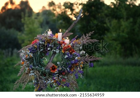 Flower wreath with burning candles on evening meadow. floral festive decor, symbol of Summer Solstice Day, Midsummer, Litha sabbat. pagan folk traditions, wiccan rituals, witchcraft. copy space
