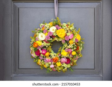 Flower Wreath Hanging On A House Wooden Door. Fresh Wild Flowers And Herbs, Home Decoration, Front View. Spring Sunny Day. Women Or Mothers Day Celebration