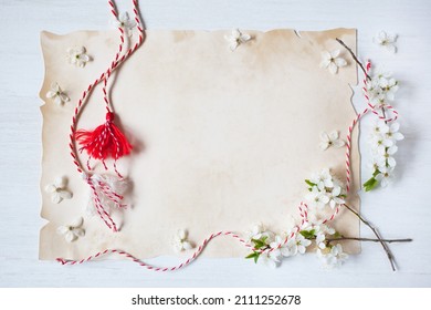 Flowering branches of cherry plum, red-white martenitsa with tassels and paper for text for the holiday of March 1, white wooden background.