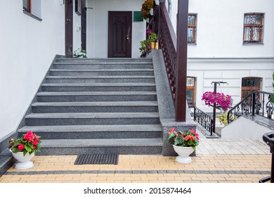 flowerpots with flowers at the staircase of the front porch with doors of the building faced with granite stone with wooden railings the exterior of the backyard architecture with bushes, nobody. - Powered by Shutterstock