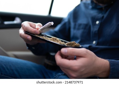 Flowers Of Cannabis. Grinder And Shredded Cannabis Joint Packet Of Weed On A Car Background Close Up Marijuana Joint In Hand Bud