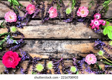 Flowers In A Circle On A Wooden Background. Postcard For The Holiday. Roses, Geraniums, Lavender, Sage And Hairy Chestnuts Are Placed Along The Edges On Dark Boards. Background Copy Space, Flat Lay