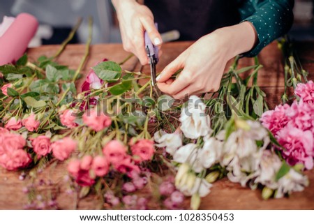 Flowers delivery, creating order. Woman florist hands closeup, cuts rose for bouquet in flower shop.