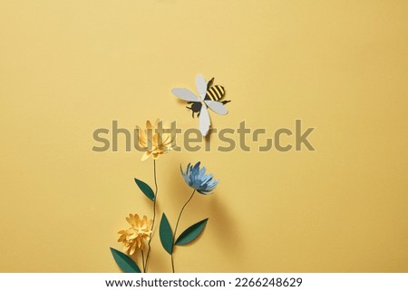 Flowers with many colors and a paper bee on light yellow background. Empty area for product or text. Graphic design for spring
