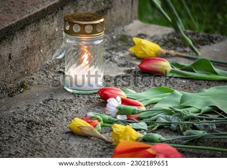 Flowers on granite gravestone of WWII soldiers with burning candle on Victory Day May 9