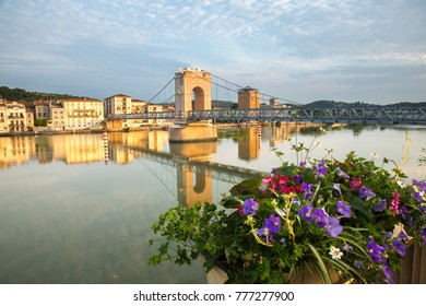 Flowers on the sea wall and the Place de Saint Colombe bridge across the Rhone River in Vienne, France