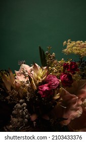 Flowers on a solid green background with space for copy. Moody feeling. Dark tone vertical picture with flower arrangement.