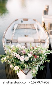 Flowers on white rowboat, floral arrangement decoration on small row boat on dock in lake or pond, wedding flower bouquet in wooden boat