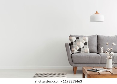 Flowers on wooden table and grey settee in white living room interior with copy space. Real photo - Shutterstock ID 1192353463