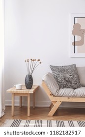 Flowers On Wooden Table Next To Beige Couch With Cushion In Flat Interior With Poster. Real Photo