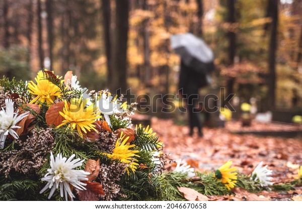 Flowers at tombstone. Defocused mourning\
woman holding flowers in hands and standing at grave in cemetery.\
Paying respect and last goodbye for dead\
person