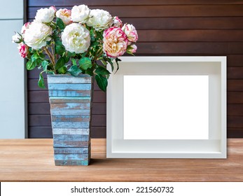 Flowers Vase And Blank White Picture Frame On Wooden Desktop
