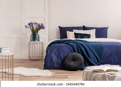 Flowers in vase on bedside table next to king size bed with navy blue bedding