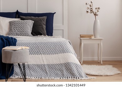 Flowers In Vase On Stylish Nightstand Table Next To Comfortable Bed With White And Blue Bedding