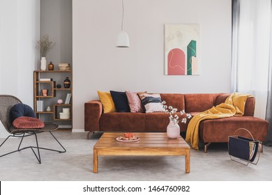 Blumen in Vase auf einem Holztisch im modernen Wohnzimmer mit braunem Ecksofa mit Kissen und abstraktem Gemälde an der Wand