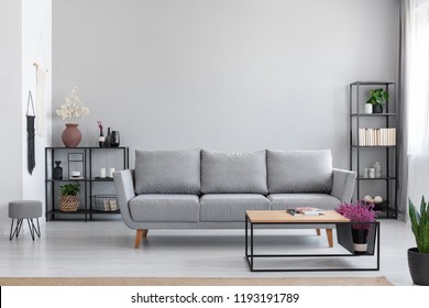 Flowers in wooden table in front of grey settee in modern simple apartment interior with stool. Real photo - Shutterstock ID 1193191789