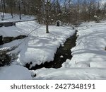 Flowing stream next to an old springhouse covered in fresh snow on a rural property in Pittstown, Union Township, New Jersey, USA