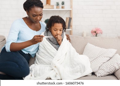 Flu Concept. Worried Black Mother Checking Her Daughter's Temperature, Child Covered In Blanket, Copy Space