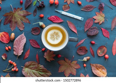 Flu Season, Cold Concept. Autumn Coloured Leaves, Ripe Rosehip Berries With A Cup Of Hot Tea With Lemon, Mercury Thermometer With High Temperature On Blue Background, Flat Lay, Top View. Fall Leaves. 