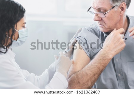 Flu Vaccine. Close up of young latina nurse giving elderly male patient injection in hospital room, copyspace