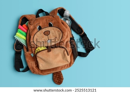 Fluffy  backpack shape of beaver with school supplies on blue background. Top view