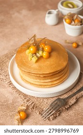 Fluffy stack of pancakes topped with fresh kiwi slices and orange cape golden berries 