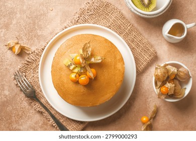 Fluffy stack of pancakes topped with fresh kiwi slices and orange cape golden berries 