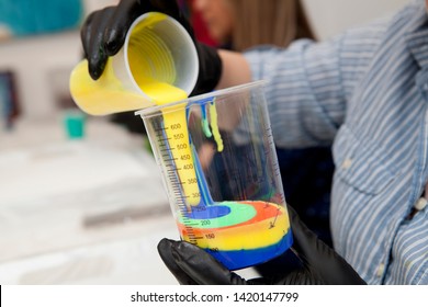 In a fluid pour painting class, a student mixes bright yellow into her colorful psychedelic pallete of neon orange, blue, and turqouise acrylic paints to be used in her dirty pour method of making art