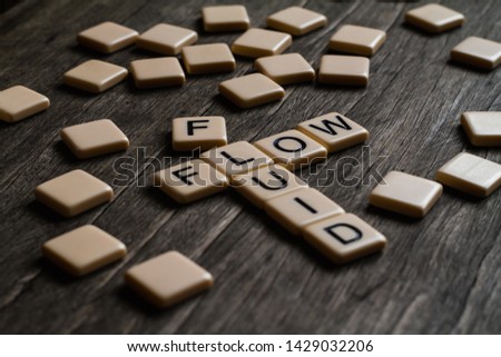 Fluid/flow affirmation spelt out using tiles on a timber surface