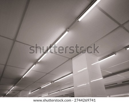 Fluorescent ceiling lights installed in a modern commercial building interior. Minimalist architectural design with geometric perspective lines.