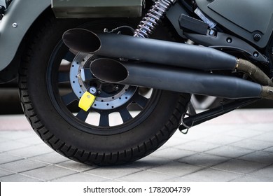 Fluorescent yellow anti-theft padlock attached to the rear disc brake of a gray motorcycle with two tailpipes