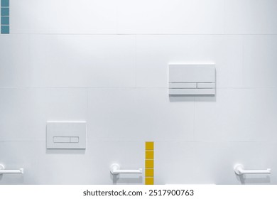 Flush buttons on a minimalist white-tiled wall in a public restroom, with small accents of blue and yellow tiles, creating a clean and modern interior design. - Powered by Shutterstock