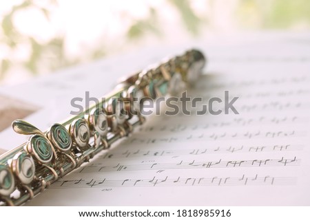 Flute, woodwind brass instrument in classical orchestra. Silver modern flute on white sheet music note for education and performance. Song composer on papers sway by wind.
