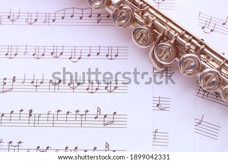 Flute, woodwind brass instrument in classical orchestra. Silver modern flute on white sheet music note for education and performance. Song composer on score sheet for orchestra.