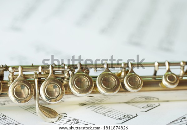 Flute, woodwind brass\
instrument in classical orchestra. Silver modern flute on white\
sheet music note for education and performance. Song composer on\
paper with instrument.