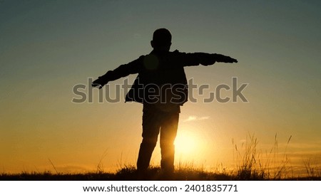 Fly concept, Child boy play like an airplane, in park opposite sky at sunset. Boy aviator dreaming raised his hands to wings of plane on field in rays of sun. Child wants to become an astronaut pilot