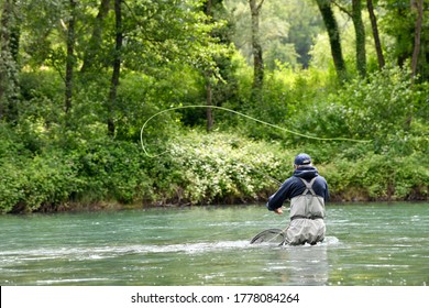 fly fisherman with black jacket fishing in the middle of the river in a mountain river in summer - Powered by Shutterstock