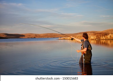 Fly Fisherman Casting In A Lake In Golden Light.