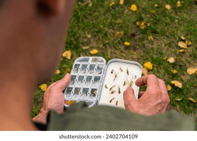 Fly fisherman chooses artificial flies from lures box for fly fishing at river - Powered by Shutterstock