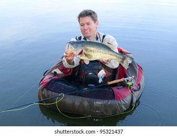 Fly Fisherman In Pontoon, Float Tube Or Belly Boat, With Large Largemouth Bass Caught Fishing With Fly Rod