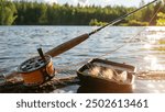 A fly fishing rod and an open fly fishing box lie on the rocks of a mountain river.