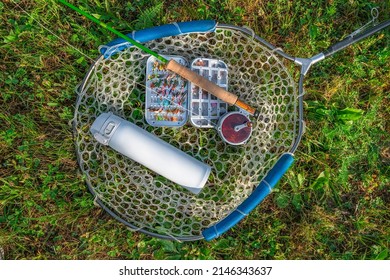 Fly Fishing Tackle. Tackle Box With Flies, Rod, Reel And Thermo Water Bottle On Fishing Landing Net.