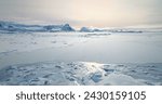 Fly over frozen Antarctic ocean sunset landscape. Snow covered untouched wilderness of South Pole. Desert white land of snow and ice aerial drone shot. Mountains in background. Nature conservation