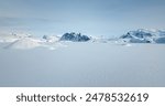 Fly over snow covered arctic winter landscape, towering mountains in background. Aerial view of frozen Antarctica panorama under blue sky in sunny day. Polar frozen ocean. Low angle aerial drone shot