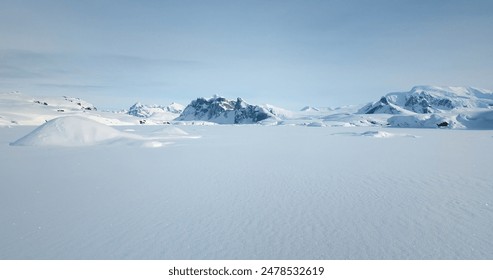 Fly over snow covered arctic winter landscape, towering mountains in background. Aerial view of frozen Antarctica panorama under blue sky in sunny day. Polar frozen ocean. Low angle aerial drone shot - Powered by Shutterstock