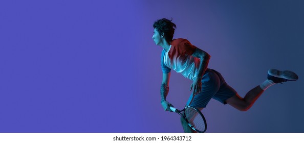 Flyer. Young caucasian man playing tennis isolated on purple-blue studio background, action and motion concept. Fit professional sportsman training, practicing in neon light. Copyspace for ad. - Shutterstock ID 1964343712