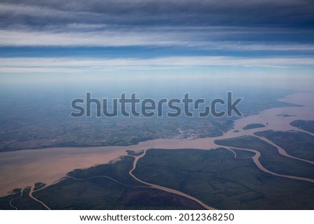 Flying. Aerial view of the Amazon river, streams and tributary channels flowing across the green tropical rainforest and field, under a beautiful blue sky. 