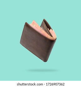 Flying in air Brown genuine leather wallet with banknotes and credit card inside isolated on turquoise background.